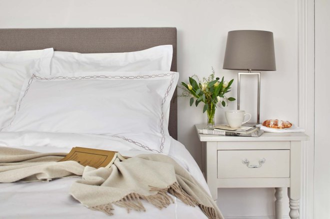 Double bed with some white bedlinen, a camel throw and a reading book.